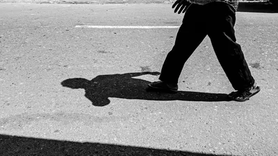 Schwarzweißaufnahme einer Person und ihres Schattens auf der Straße