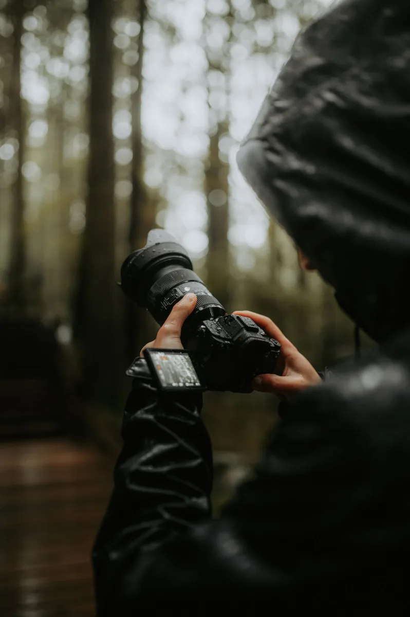 Person hält eine Kamera mit beiden Händen im Wald
