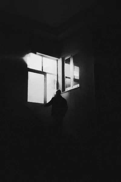 Dunkler Raum mit Person als Silhouette am Fenster