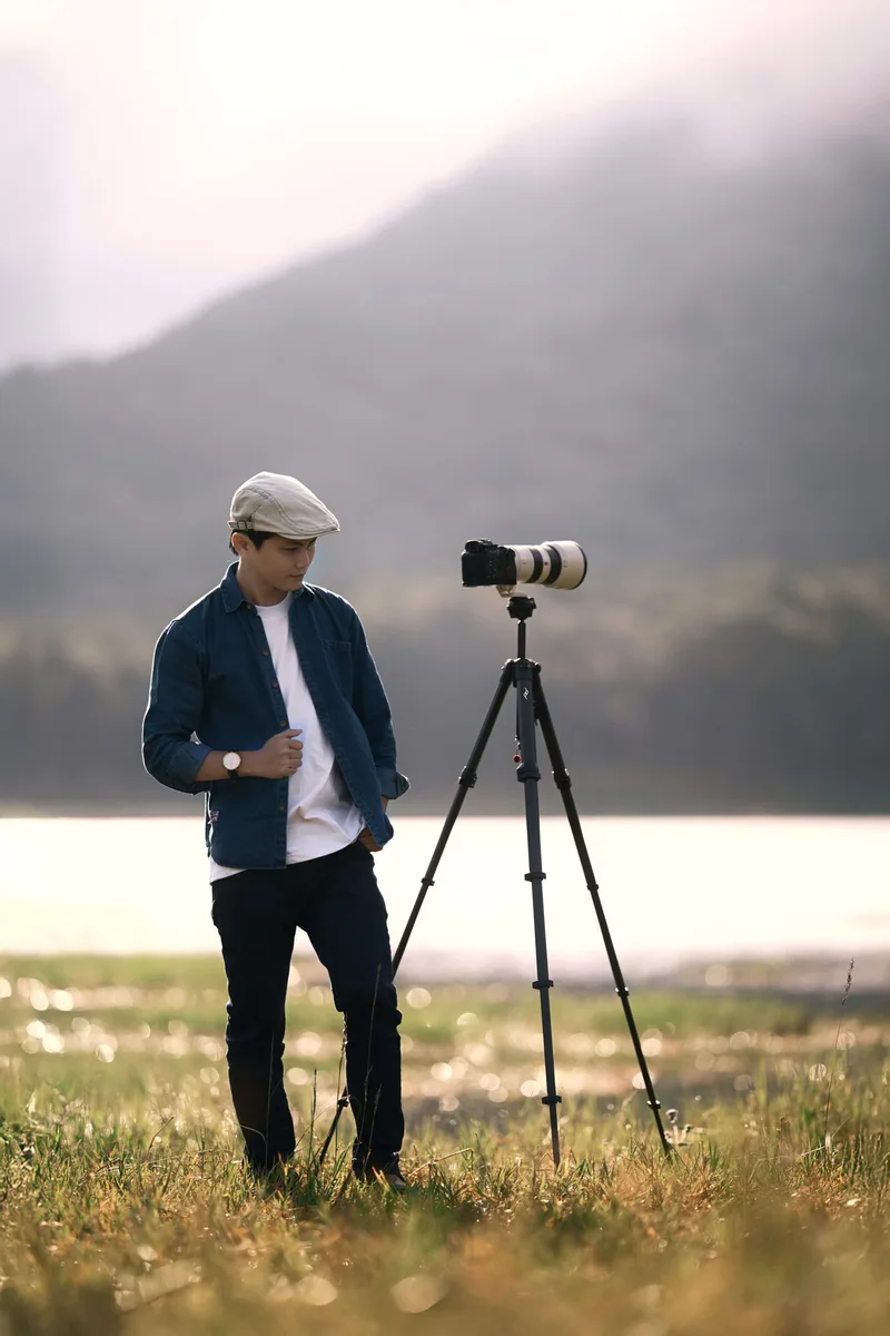 Fotograf mit Kamera und Stativ in einer Landschaft